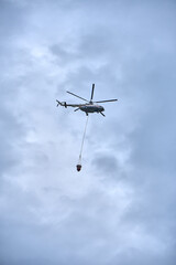 Fire fighting helicopter with water bucket on a gloomy sky background