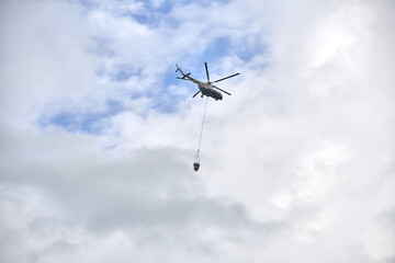 Fire fighting helicopter with water bucket on a cloudy sky background