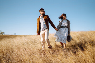 Stylish  young couple enjoying autumn weather in autumn field. Lovely couple walking and hugging in the field together. The concept of youth, love and lifestyle.