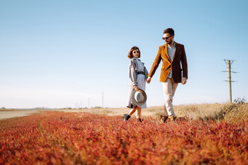 Young loving couple walking and hugging in autumn field. Enjoying time together. Fashion, lifestyle and autumn mood.