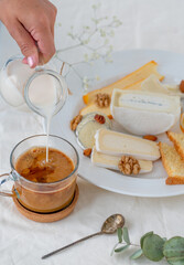 The moment of pouring milk into coffee on the background of a cheese plate