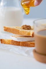 toast with soft cheese, nuts, honey, milk and a Cup of coffee. Breakfast at the white table.