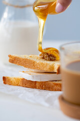 toast with soft cheese, nuts, honey, milk and a Cup of coffee. Breakfast at the white table.