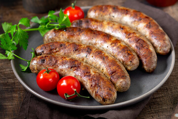 Fried sausages. Grilled sausages with spices, sauce, tomatoes and parsley. Delicious meat sausages in a ceramic plate	