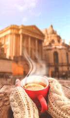 Autumn background, hot cup of tea. Red cup in female hands on the background of the autumn landscape, autumn city. Sunlight, wooden table.