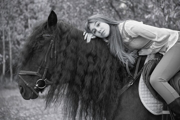 A black and white photo of a girl with long hair sitting on a horse with a thick mane .