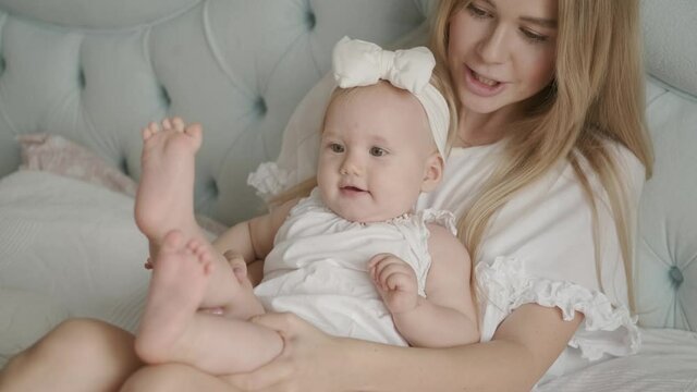 Portrait of a little cute girl. The child sits on his mother's lap and plays. A young mother holds the plump legs of her pretty daughter. Family happy. New parent with their baby