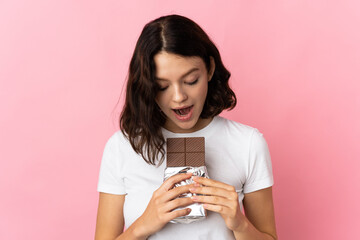 Teenager Ukrainian girl isolated on pink background eating a chocolate tablet
