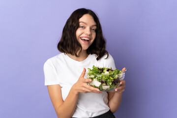 Teenager Ukrainian girl isolated on purple background holding a bowl of salad with happy expression