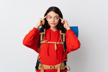 Teenager mountaineer girl with a big backpack isolated on white background having doubts and thinking