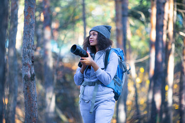 African American woman walking in the forest with a photocamera.