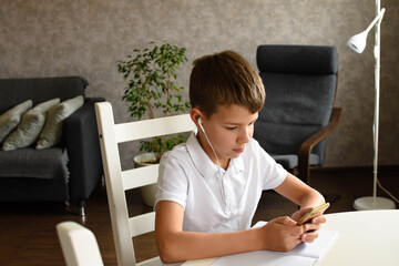Naklejka premium A boy with headphones looks at the phone. Home schooling