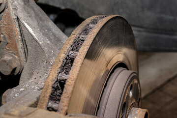Old front brake disc with caliper and brake pads in the car, on a car lift in a workshop, close-up of a brake disc.