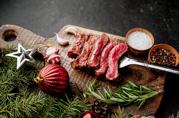 Different degrees of roasting of steak on a meat fork for Christmas on a background of a stone with a spruce and Christmas toys 