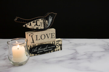 Love Bird with Love Quote next to a lit Candle on a marble table.