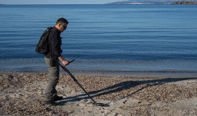 
man uses the metal decector at the beach to search for precious objects