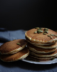 delicious homemade american pancakes with sweet syrup and pumpkin seeds on black background close up