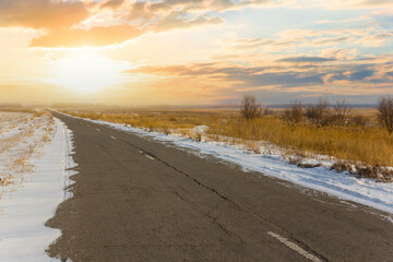 asphalt road among a snowbound prairie at the sunset