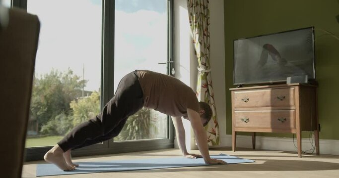 Young adult male practicing yoga exercise at home watching tutorial on television during lockdown pandemic