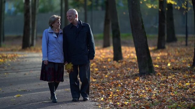 old woman is walking with her husband in park at fall day, spouses are enjoying good weather