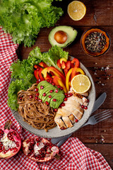  Healthy buddha bowl lunch - soba noodles with chicken, avocado and vegetables on a textured wooden background, top view, vertical photo