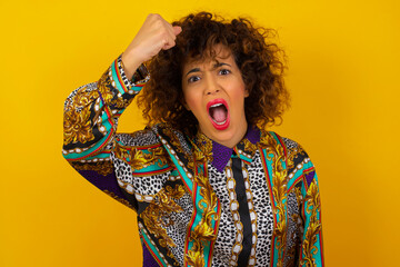 Fierce confident European dark-haired woman holding fist in front of her as if is ready for fight or challenge, screaming and having aggressive expression on face. Isolated over gray background.