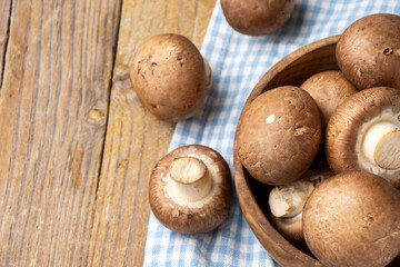 Aerial view of portobello mushrooms in wooden bowl, with selective focus, on blue checkered cloth, on rustic wooden table, horizontal, with copy space