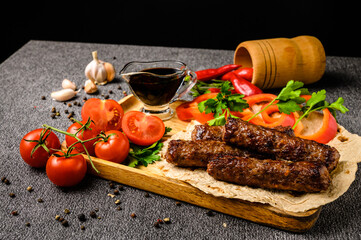 Grilled sausages are served with fresh herbs, garlic, tomatoes, red pepper and sauce in a wooden bowl. A close-up picture