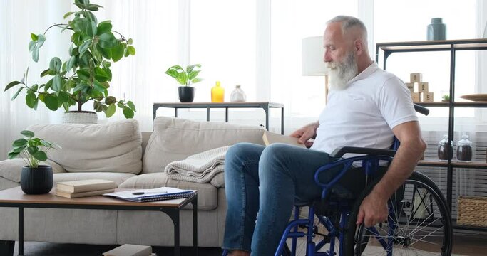 Handicap old man reading a book and stretching sitting on wheelchair at home
