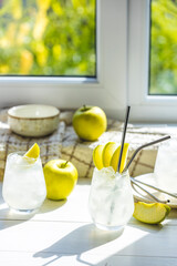 Summer cocktail with green apple and ice on the white table near window in the sunny summertime. Selective focus image with copy space
