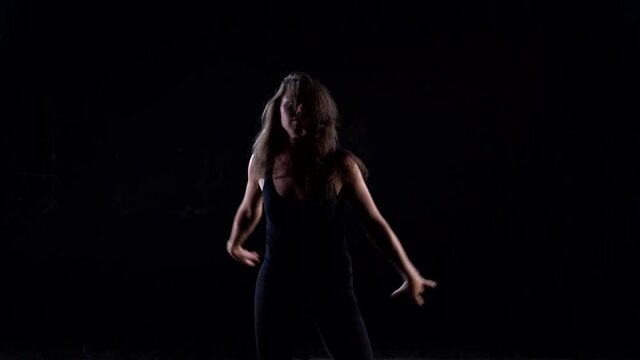 modern choreography and dance of young slender woman, dancer is moving in black background