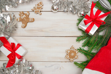 Two gift boxes with red ribbons on a light wooden background, ginger shaped cookies and Christmas tree branches. Concept of New Year and Christmas, gifts, holiday. Top view, copyspace.