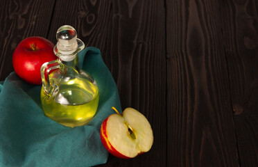 Apple cider vinegar in a glass decanter on a dark wooden table. Apples nearby. Free space.