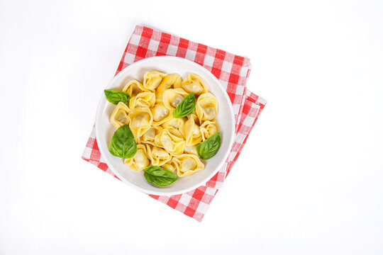 Italian tortelloni on a white plate over red checked tablecloth. top view.