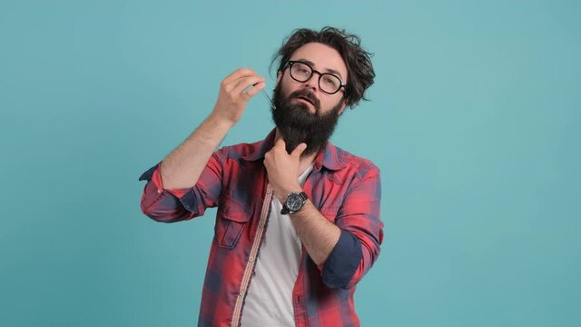 A bearded man applies his beard care oil, isolated on a turquoise background. Hair care concept.