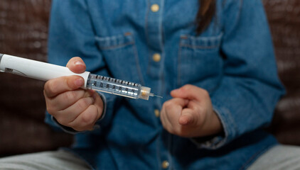 A little girl is holding a syringe with insulin. The girl injects herself. World Diabetes Day.