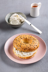 Bagel with cream cheese. Breakfast sandwich on pink plate on gray background.