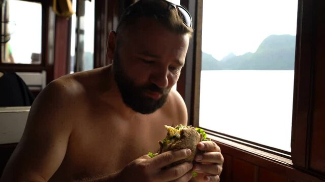 Young happy man eating tasty sandwich on the boat
