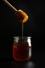 Honey jar with dipper and flowing honey on the black background