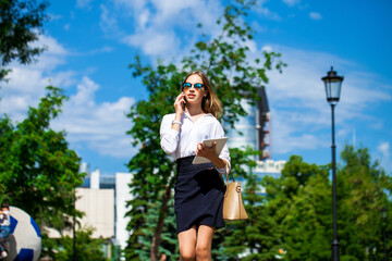 Obraz premium Young assistant in a white blouse phoning on the street