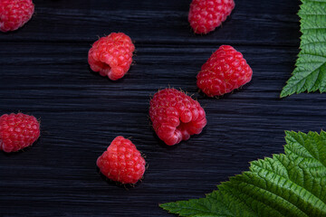 Fresh beautiful, red raspberries on a dark wood background. Green leaves. Place for text
