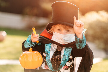 Happy Halloween. A child in a medical mask in a dracula costume sits on a pumpkin in his yard.