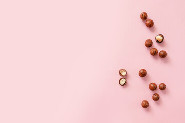 Cracked macadamia nuts on pink background, top view with copyspace.