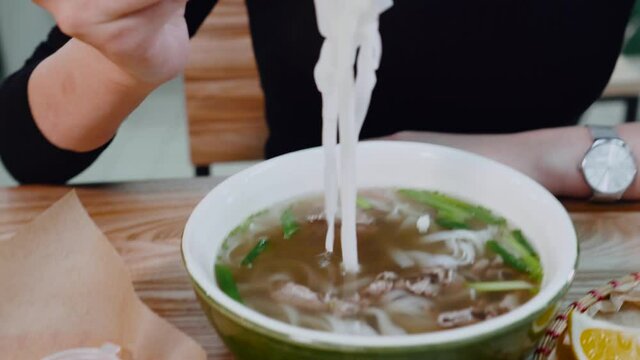 Butiful young woman eating traditional asian Thai noodles with chopsticks. Girl feel hungry and enjoy fast food night meal