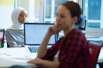 Multiethnic colleagues dark haired caucasian and african muslim Handsome businesswomen (employee) working on a laptop in a modern startup company