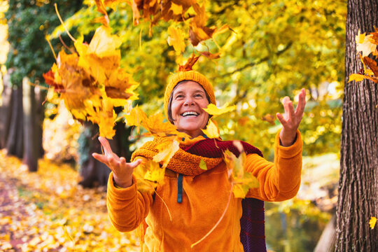 woman in her 50s outside in autumn playing with falling leaves