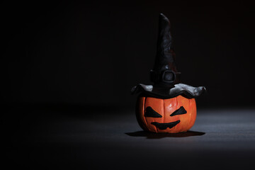 Cabeza de calabaza con ojos, boca y  sombrero de bruja sobre fondo negro y espacio para agregar...