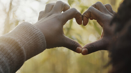 Young african man making heart shape with his hands in the woods. High quality photo