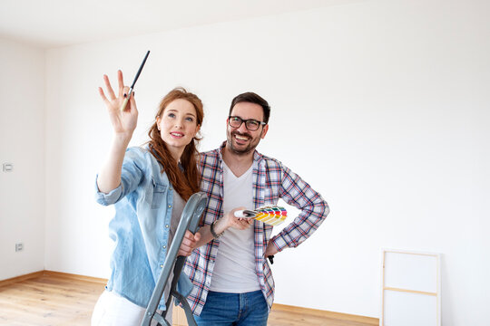 Couple in new house plan how to paint walls and looking at samples of colours with brushes on hand