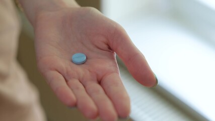 Close-up of the open palm of a girl holding a blue pill without packaging.